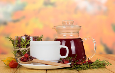 Jug with of broth hips, dried berries in jar and spoon, on table