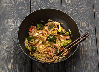 Asian dish of meat, vegetables and noodles with spices in wok, on background of table