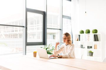 Happy young business woman sitting in office using laptop