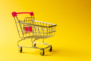 Close up of supermarket grocery push cart for shopping with black wheels and red plastic elements on handle isolated on yellow background. Concept of shopping. Copy space for advertisement