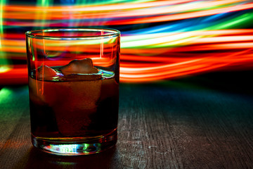 Glass of whiskey on the table. Multicolored blurred stripes.