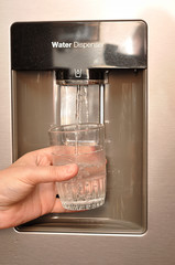 A woman’s hand holding a glass, and water pouring in to it out of a water dispenser