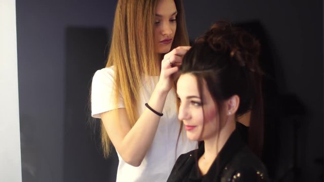 Young blonde stylist girl makes hairstyle to a woman