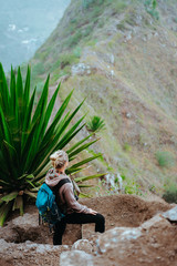 Naklejka na ściany i meble Woman with backpack on the trekking route near mountain edge looking down to valley. Santo Antao island, Cabo Verde