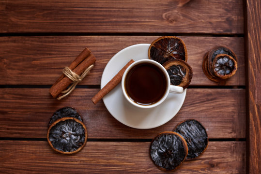 Чашка кофе с сушеными дольками лимона и палочками корицы на деревянном коричневом фоне