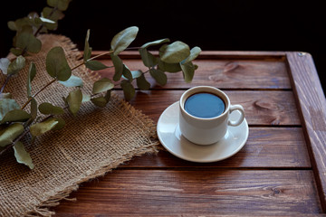 Чашка кофе с дымком, ветками эвкалипта, салфеткой из мешковины на деревянном коричневом фоне