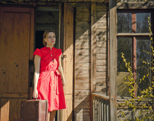 near the old wooden house girl in a red dress with a suitcase