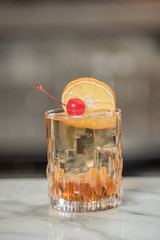 cocktail glass of whiskey with ice decorated with pickled cherries and a slice of orange