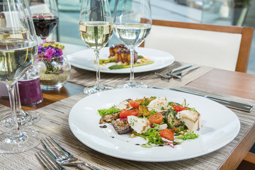 Lunch at the restaurant. White wine in a glass and a warm salad with greens, cherry tomatoes, cheese and aubergines grilled.