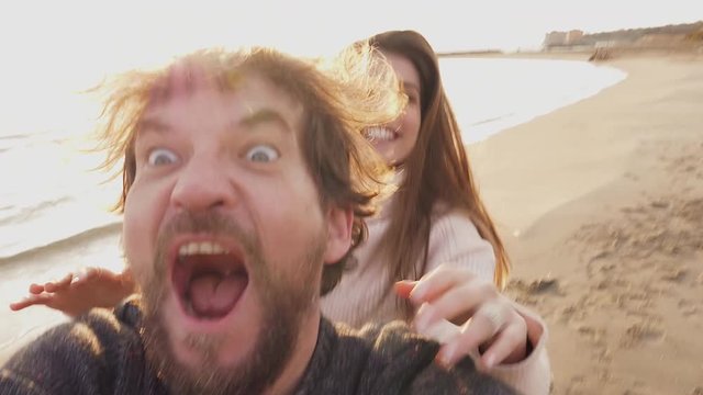 Happy couple doing funny selfie video running on beach