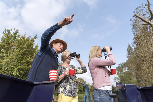 Group Of People On A Boating Holiday Using Binoculars To Spot Wildlife Along The Wilts & Berks Canal At Swindon UK