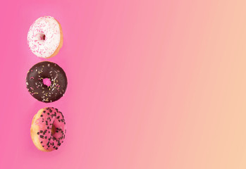 Fototapeta na wymiar Colorful glazed donuts in motion on pink background.