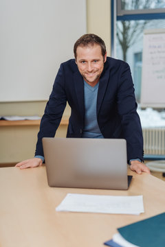 Smiling man standing over desk with laptop