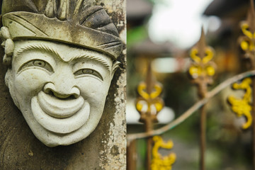 Head of a Hindu deity stone statue of a person with a smile on the background of a fence. Travels...