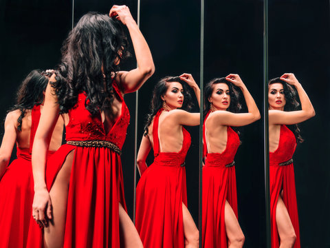 Portrait of beautiful brunette woman in red shoes and dress standing near the mirrors