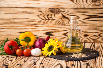 Glass bottle of sunflower oil on a wooden table with a composition of vegetables and seeds