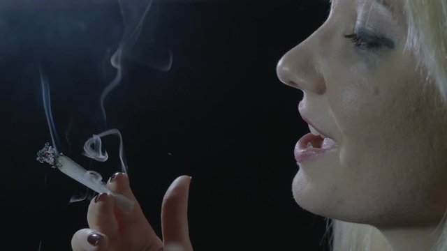 Drug addicted blonde woman with blue eyes lightning a marijuana joint smoking it and relaxing