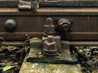 Detail of rusty screws and nut on old railroad track. Concrete tie with rusty nuts and bolts. Damaged surface of rail rod. No train passed this railroad for a long time.