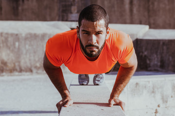 Concentrated young man doing push-ups on curb