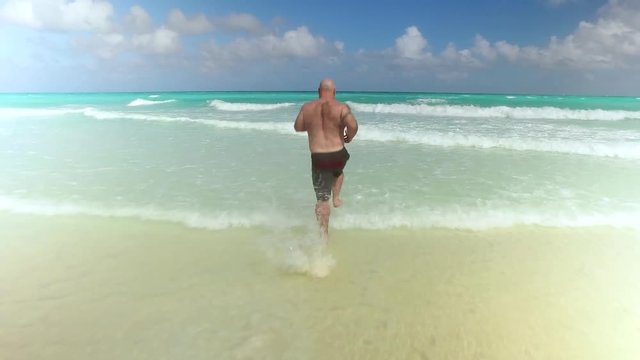 A man in his 40s runs and dives into the water on a beautiful white sands beach.