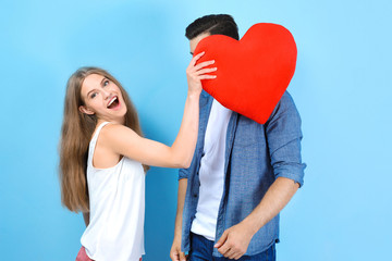 Young couple holding pillow in heart shape on light background