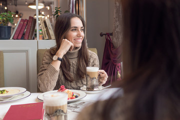 A young woman talking to a friend drinking coffee and eating dessert.