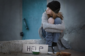 Homeless poor teenage girl sitting outdoors near empty bowl and piece of cardboard with word HELP