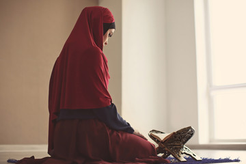 Young Muslim woman reading Koran, indoors