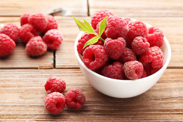 Ripe raspberries in bowl on brown wooden table