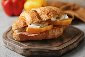 Tasty croissant sandwich on wooden board
