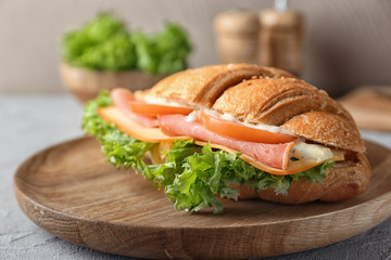 Tasty croissant sandwich on wooden plate