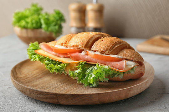 Tasty croissant sandwich on wooden plate