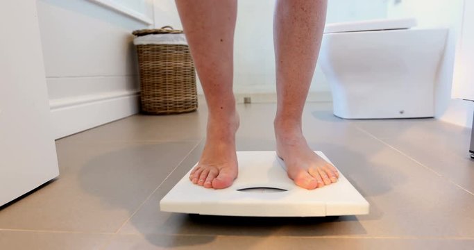 Low section of woman checking her weight on weighing scale 