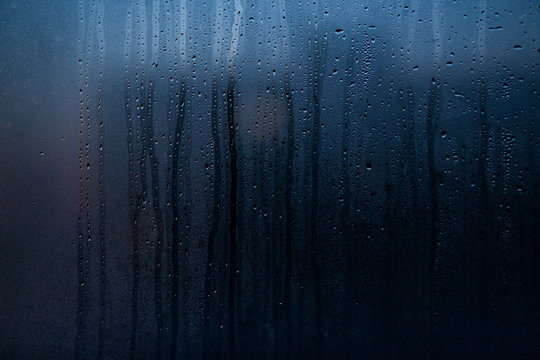 Flowing down water drops on window glass