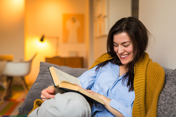 Woman sitting on sofa and reading book at her home