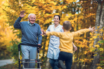 Cheerful disabled grandfather in walker welcoming his happy grandson