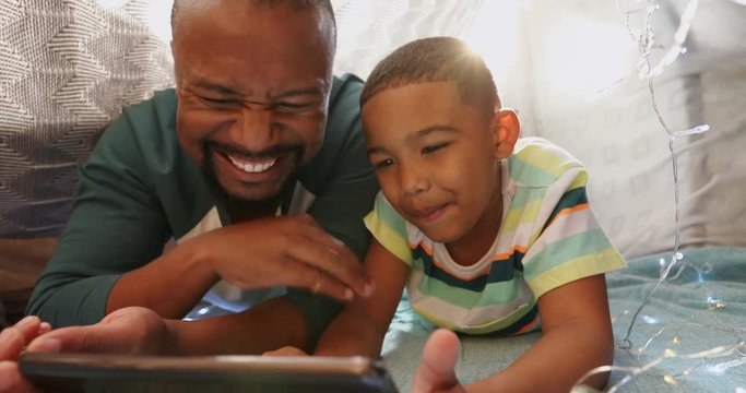 Father and son using digital tablet in bedroom