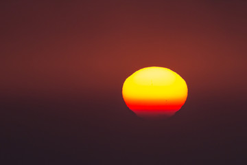 red big sun obscured by clouds near the horizon at sunset or sunrise. The sun is partially seen through the clouds 