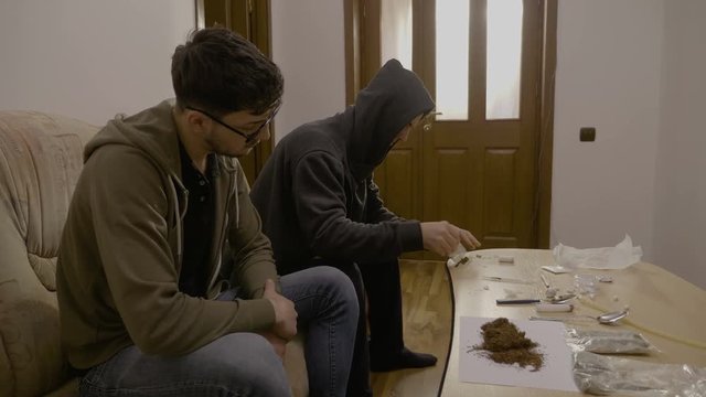 Young men sitting in the living room on the couch rolling weed in paper to smoke joints while the parents are not home