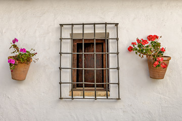 Fototapeta na wymiar Detail of Spanish white house facade with fenced window and flower pots on the white wall.