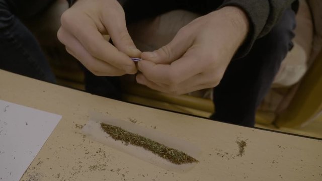 Close up of a junkie man hands rolling the perfect weed joint filter and then using his tongue to stick the cigarette paper