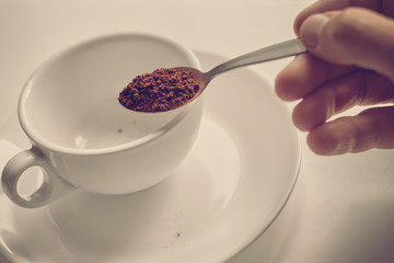 Hand pouring instant coffee from spoon in cup, image with warm vintage toning