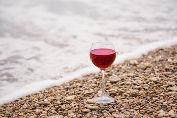 A glass of red wine on the pebble beach at the sea coast. Vacation pleasure concept