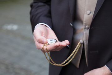 Hand eines elegant gekleideten Mannes hält Taschenuhr