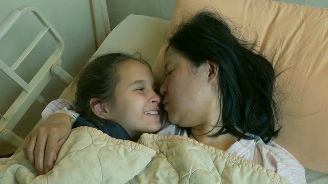 Happy child kissing mother in hospital bed