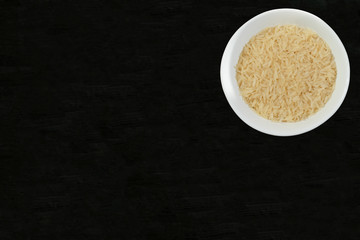 Rice in white bowl on black background, top view. Space for your text