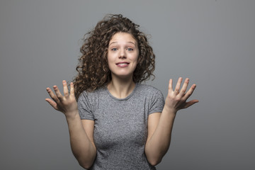 portrait of a young curly woman, surprised by a good news on gray background