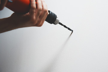 Drilling in the wall. The man is holding a screwdriver or drill in hand. Drills a hole in the wall using a drill with a drill. Concept of housework, renovation at home, apartment.