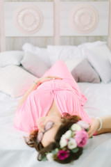 Young beautiful pregnant girl in a pink dress lying in the bed