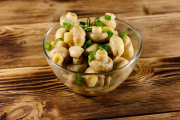 Glass bowl with pickled champignons. Marinated mushrooms on wooden table